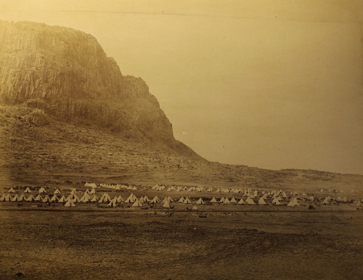 photo of tents at the foot of a huge rocky hill with sheer vertical sides..