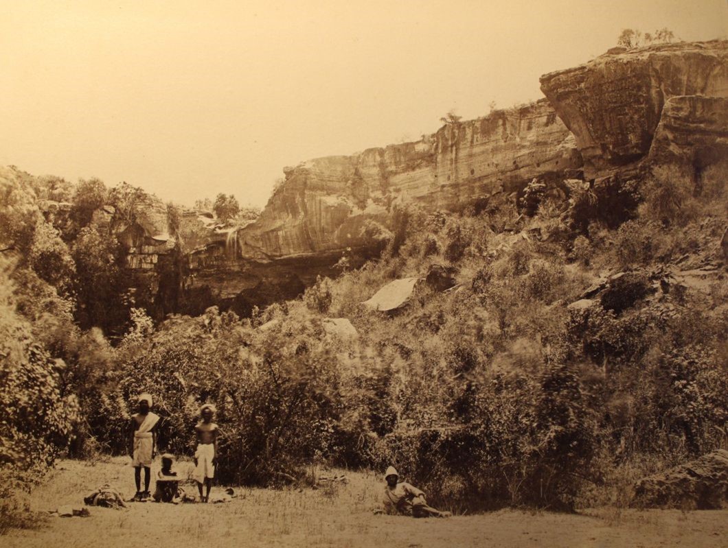photo of several men standing in front of shrubs and a small waterfall.
