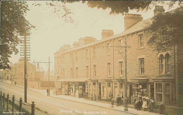 The black and white photo shows South Road around 1900. To the right is a row of Victorian three storey stone houses. They have bay windows at street level and some of them are shops.