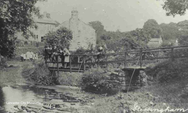 The black and white photo shows children on a footbridge over a beck at Gressingham. The photo dates from around 1900 and the girls have white pinafores and the boys are in jackets, white collars and caps.