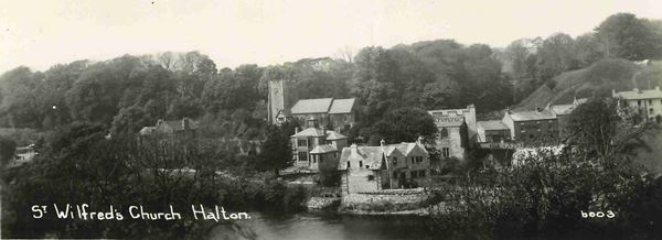 The black and white photo looks across the River Lune to Halton church rising over some old stone houses near to the river. To the right is a grassy mound, which is the old castle motte.