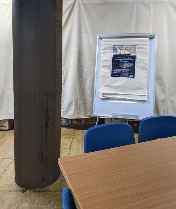 Photo of part of the education room, showing a table, flipchart and the ship's mast.