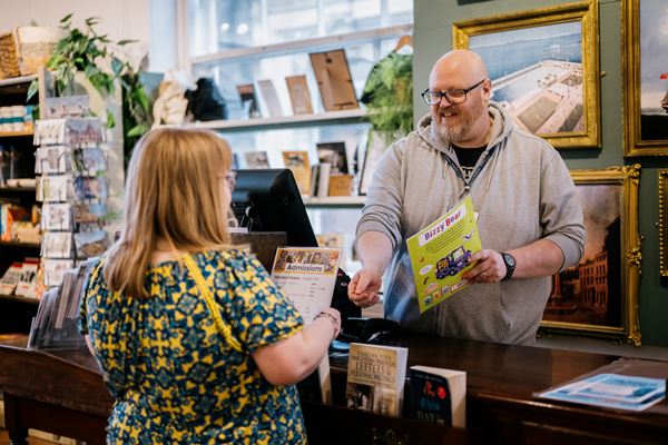 Photo of a woman buying a book from a smiling man at a wooden shop counter.